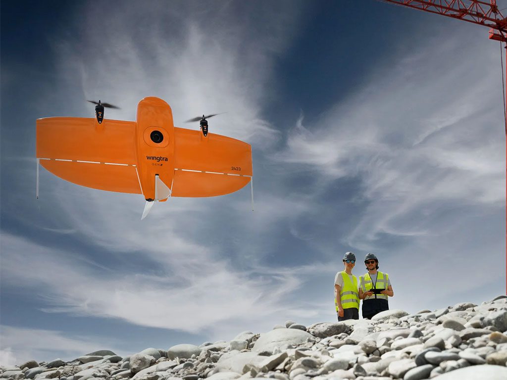 Drone orange Wingtra One Gen II volant au-dessus de deux ingénieurs sur un chantier rocheux